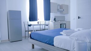 A hotel room with a bed, a desk, a chair, a refrigerator, and a kitchenette. - Naxos Laguna Beach (Giardini Naxos)