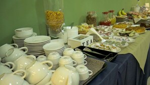 Un tavolo per buffet con diversi cibi, servizio da tè e piatti bianchi impilati.