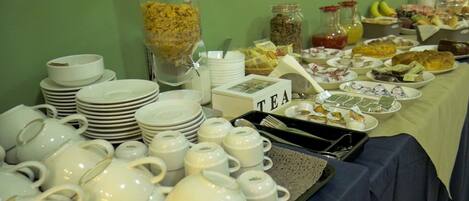 Una mesa de buffet con diversos alimentos, servicio de té y platos blancos apilados.