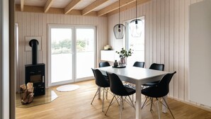 Een eetgedeelte met een grote tafel, zwarte stoelen, een houtkachel en een raam met uitzicht.