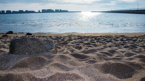 Een zandstrand met een grote rots op de voorgrond en een rustige zee op de achtergrond.