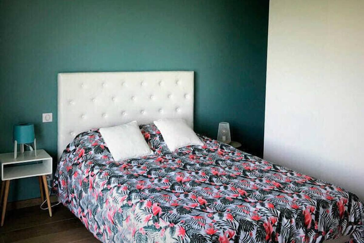 A bedroom with a tufted headboard, floral bedding, and a teal accent wall.