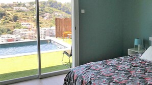 A bedroom with a large sliding glass door leading to a pool area, a bed with a patterned bedspread, and a nightstand with a lamp.