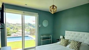 A bedroom with a large bed, a view of a swimming pool, and a balcony.