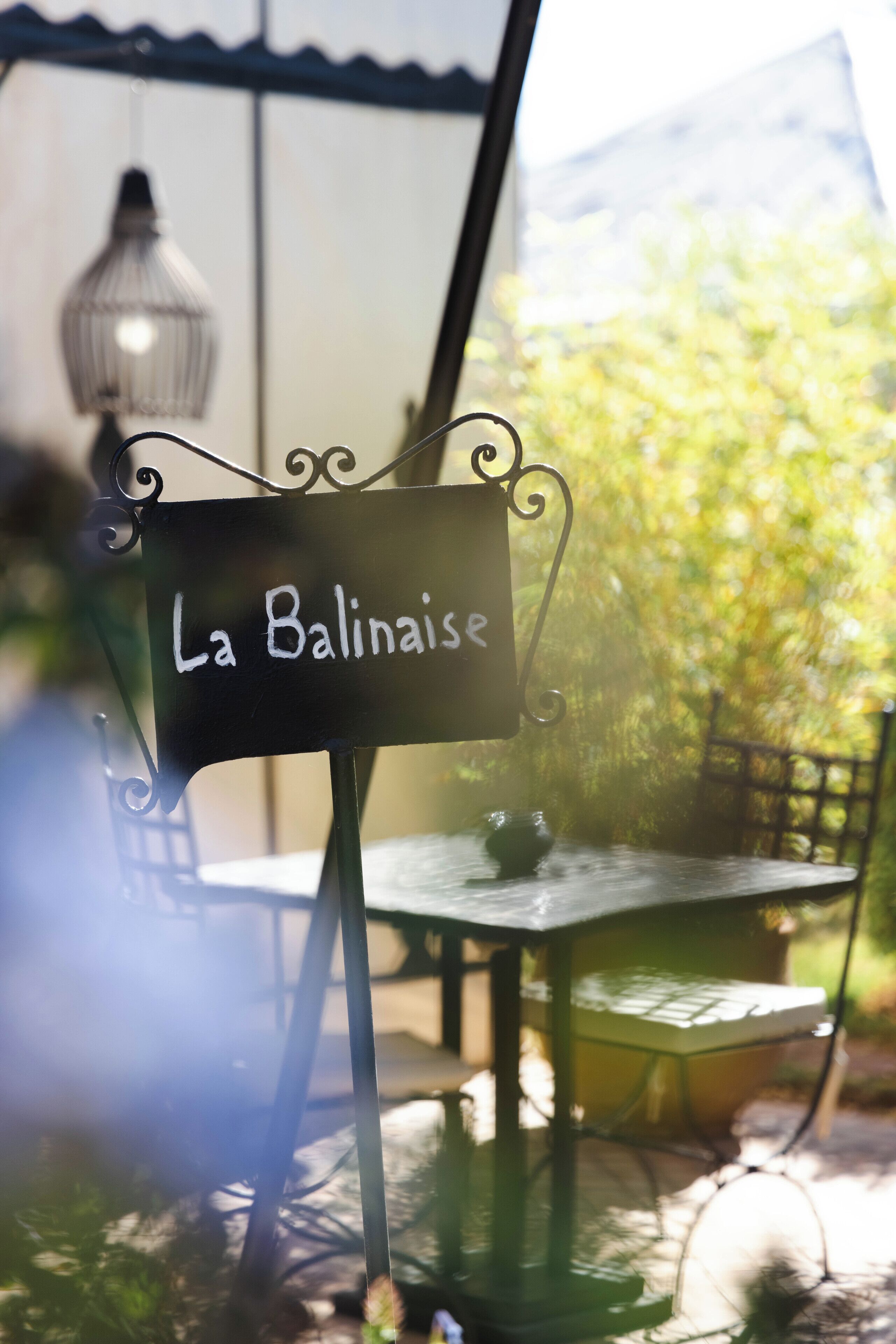 Une enseigne portant l’inscription « La Balinaise » dans un café, avec des tables à l’extérieur et un luminaire suspendu en arrière-plan.