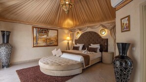 A spacious bedroom with a large bed, a round ottoman, a decorative vase, and a painting on the wall. - Eden Lodges & Spa -Boutique Hôtel de Luxe (Marrakech)