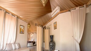 A spacious room with a large sofa, a round coffee table with decorative items, a large vase, and a bed with a canopy. - Eden Lodges & Spa -Boutique Hôtel de Luxe (Marrakech)