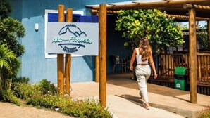 A building with a blue exterior, a signboard, and a wooden pergola. - Pousada Alto da Floresta Noronha by Alto da Ilha (Fernando de Noronha)