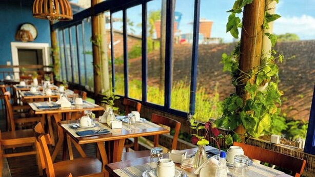 A restaurant with wooden tables and chairs, large windows, and a view of greenery. - Pousada Alto da Floresta Noronha by Alto da Ilha (Fernando de Noronha)