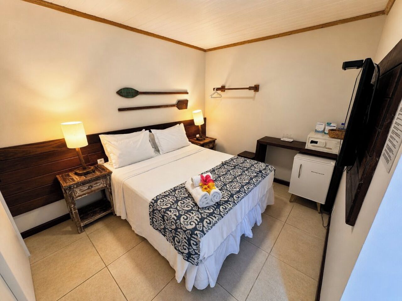 A hotel room with a bed, bedside tables, a small refrigerator, and a television.