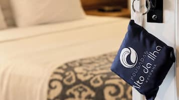 Quarto de hotel com cama, mesa de cabeceira, abajur e chaveiro com logotipo.