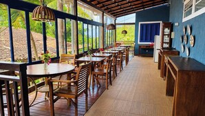 A covered outdoor dining area with wooden tables and chairs, a blue wall with decorative plates, and a view of greenery outside. - Pousada Alto da Floresta Noronha by Alto da Ilha (Fernando de Noronha)