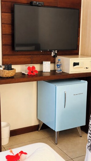 A room with a flat-screen TV mounted on a wooden wall, a small blue refrigerator, a microwave, and a basket with remote controls. - Pousada Alto da Floresta Noronha by Alto da Ilha (Fernando de Noronha)