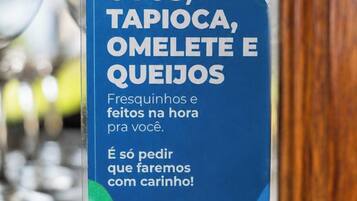 Uma caixa com texto em português, colocada sobre uma superfície de madeira com copos desfocados ao fundo.