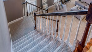 A staircase with a view of a living room, a fireplace, and large windows. - Island Life!  Kent Island Waterfront with Pool-Bring your boat! (Stevensville)
