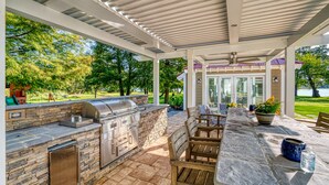 An outdoor patio with a stone barbecue and seating area. - Island Life!  Kent Island Waterfront with Pool-Bring your boat! (Stevensville)