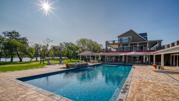 A swimming pool with a tiled deck, a covered patio area, and a large house with a balcony. - Island Life!  Kent Island Waterfront with Pool-Bring your boat! (Stevensville)
