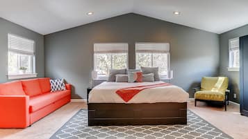 A bedroom with a large bed, a red sofa, a yellow armchair, and two windows with blinds.