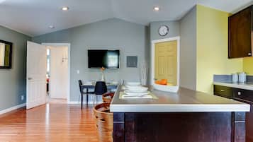 A modern kitchen with a large island, wooden chairs, a dining table, and a flat-screen TV mounted on the wall.