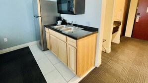 A compact kitchen with a refrigerator, microwave, double sink, and wooden cabinets. - FairBridge Inn & Suites Cuero (Cuero)
