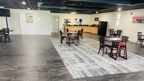 A spacious indoor area with a kitchen in the background, a dining area with chairs and a table, and a patterned rug on the floor. - FairBridge Inn & Suites Cuero (Cuero)