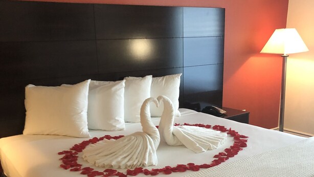 A hotel room with a large bed, white bedding, and a decorative swan made of rose petals on the bed. - FairBridge Inn & Suites Cuero (Cuero)