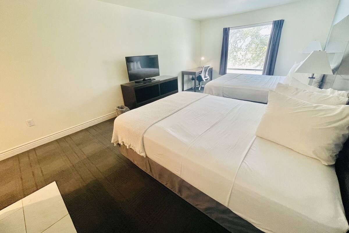 A hotel room with two beds, a TV, a desk, and a window with curtains.
