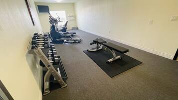 Un gimnasio con equipamiento de ejercicio, incluyendo mancuernas, un banco y máquinas de cardio.