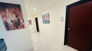 A hallway with tiled flooring, a door on the right, and paintings on the walls. - FairBridge Inn & Suites Cuero (Cuero)