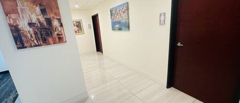 A hallway with tiled flooring, a door on the right, and paintings on the walls.