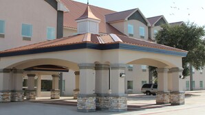 A building with a covered entrance, stone pillars, and a vehicle parked in front. - FairBridge Inn & Suites Cuero (Cuero)