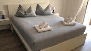 Una cama bien hecha con ropa de cama a rayas y almohadas, dos mesitas de noche con lámparas, y una ventana con cortinas.