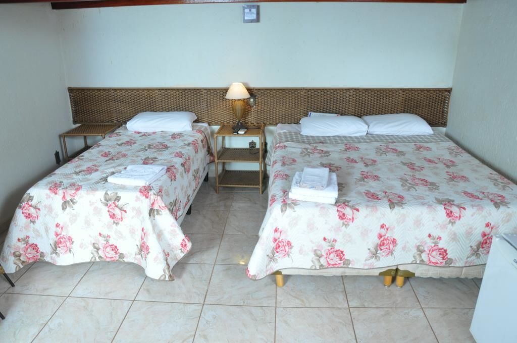 Una habitación con dos camas, cada una con ropa de cama floral y almohadas blancas. Hay una mesita de noche con lámpara entre las camas.