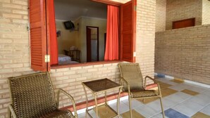A room with a brick wall, a window with red shutters, and two wicker chairs. - Pousada Beco da Lua (Olímpia)