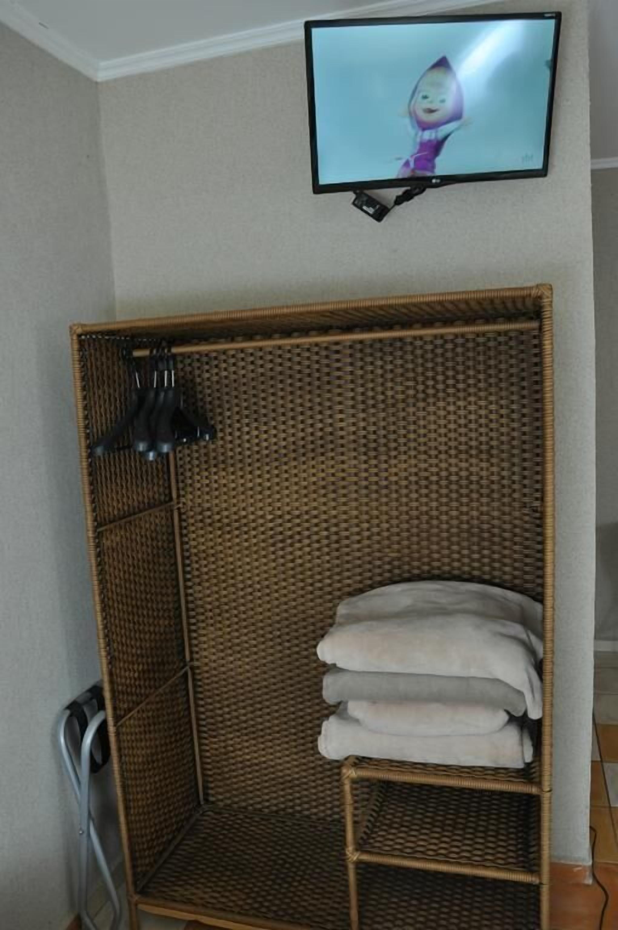 Una habitación con un sofá de mimbre, un televisor montado en la pared y una pila de toallas sobre el sofá.