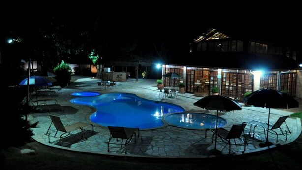 A nighttime outdoor pool area with multiple pools, lounge chairs, and umbrellas. - Pousada Beco da Lua (Olímpia)