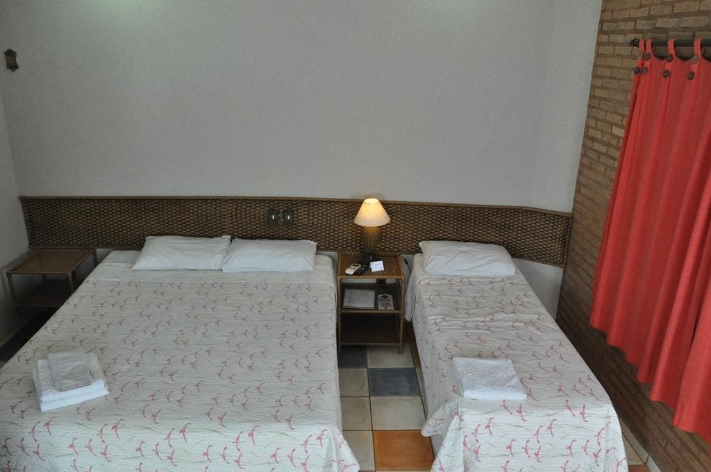 A hotel room with two single beds, a nightstand with a lamp, and a red curtain.