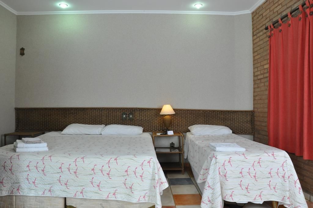 Camera d'albergo con due letti, un comodino con una lampada e una parete in mattoni.