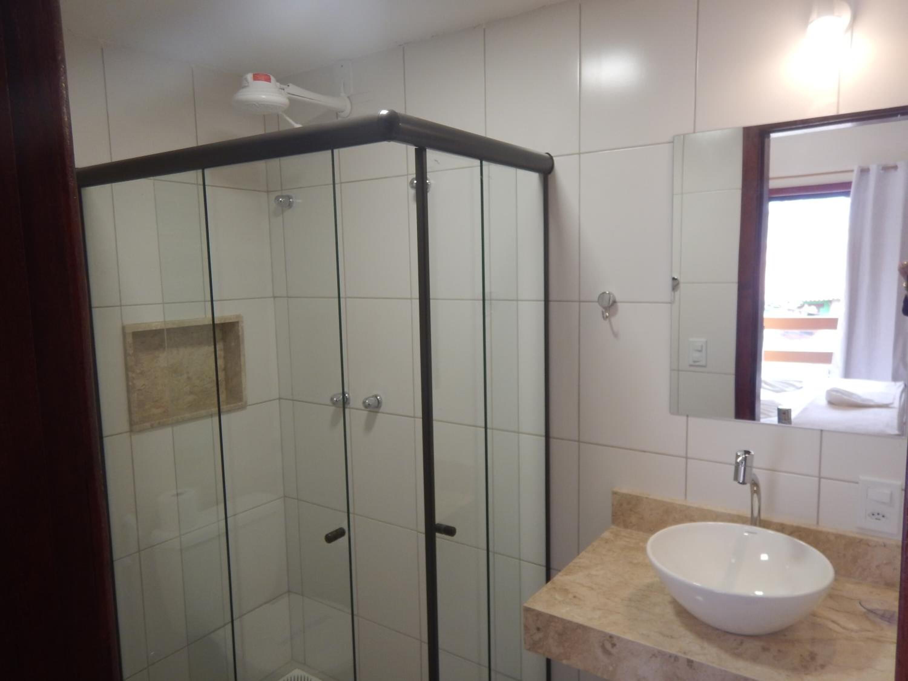 Ein Badezimmer mit einer Glaskabine zur Dusche, einem weißen Waschbecken und einem Spiegel darüber.