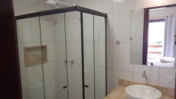 Ein Badezimmer mit einer Glaskabine zur Dusche, einem weißen Waschbecken und einem Spiegel darüber.