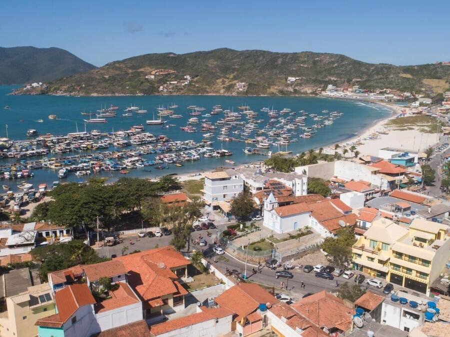 A coastal town with a marina filled with boats, buildings with red-tiled roofs, and a beach area.