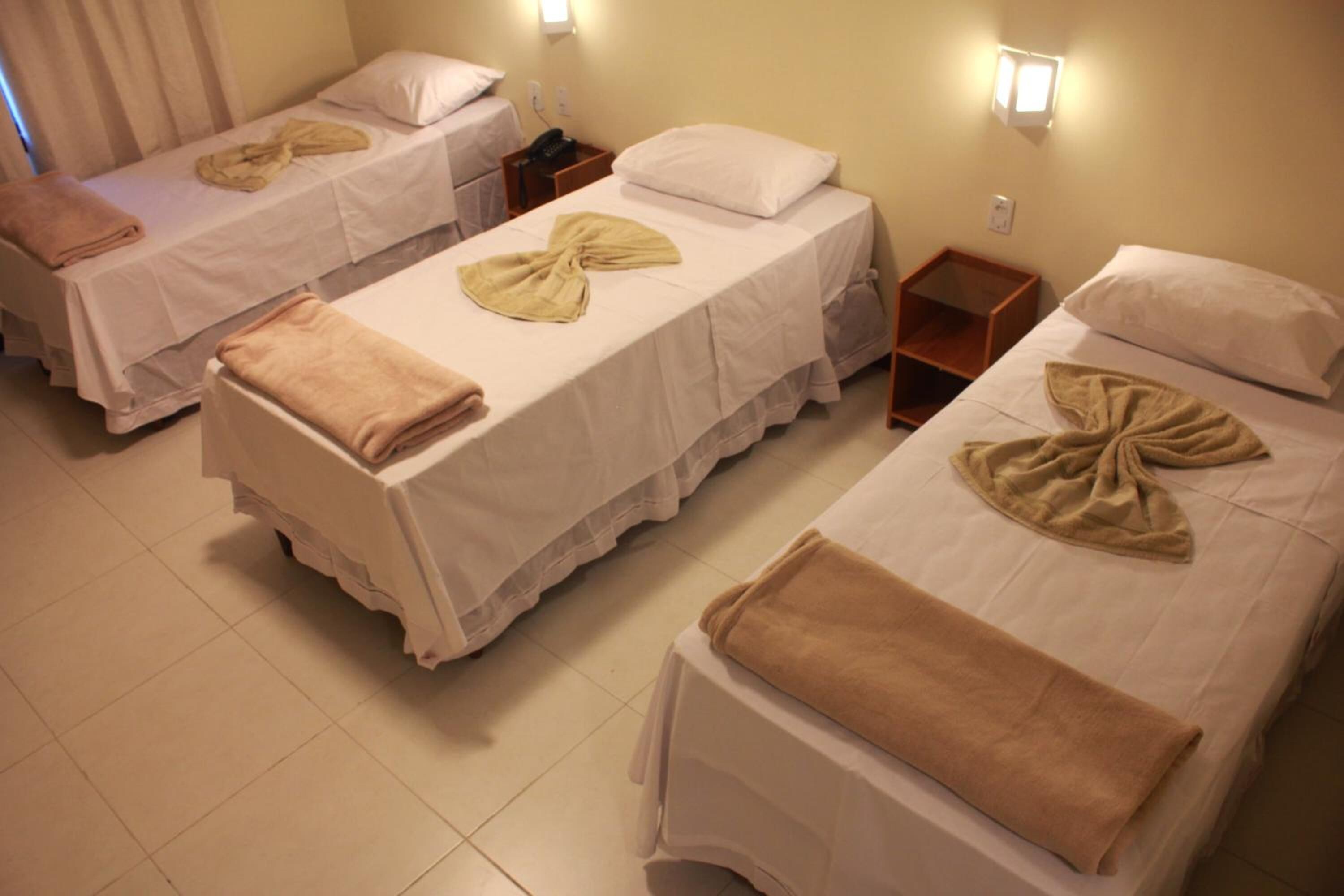 Une chambre d’hôtel avec trois lits simples, chacun étant équipé d’une serviette et d’un oreiller.