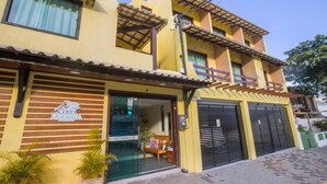 A two-story building with a yellow facade, a visible sign reading "Costa Dourada", and a covered entrance with a wooden bench and potted plants. - Costa Dourada Pousada (Arraial do Cabo)