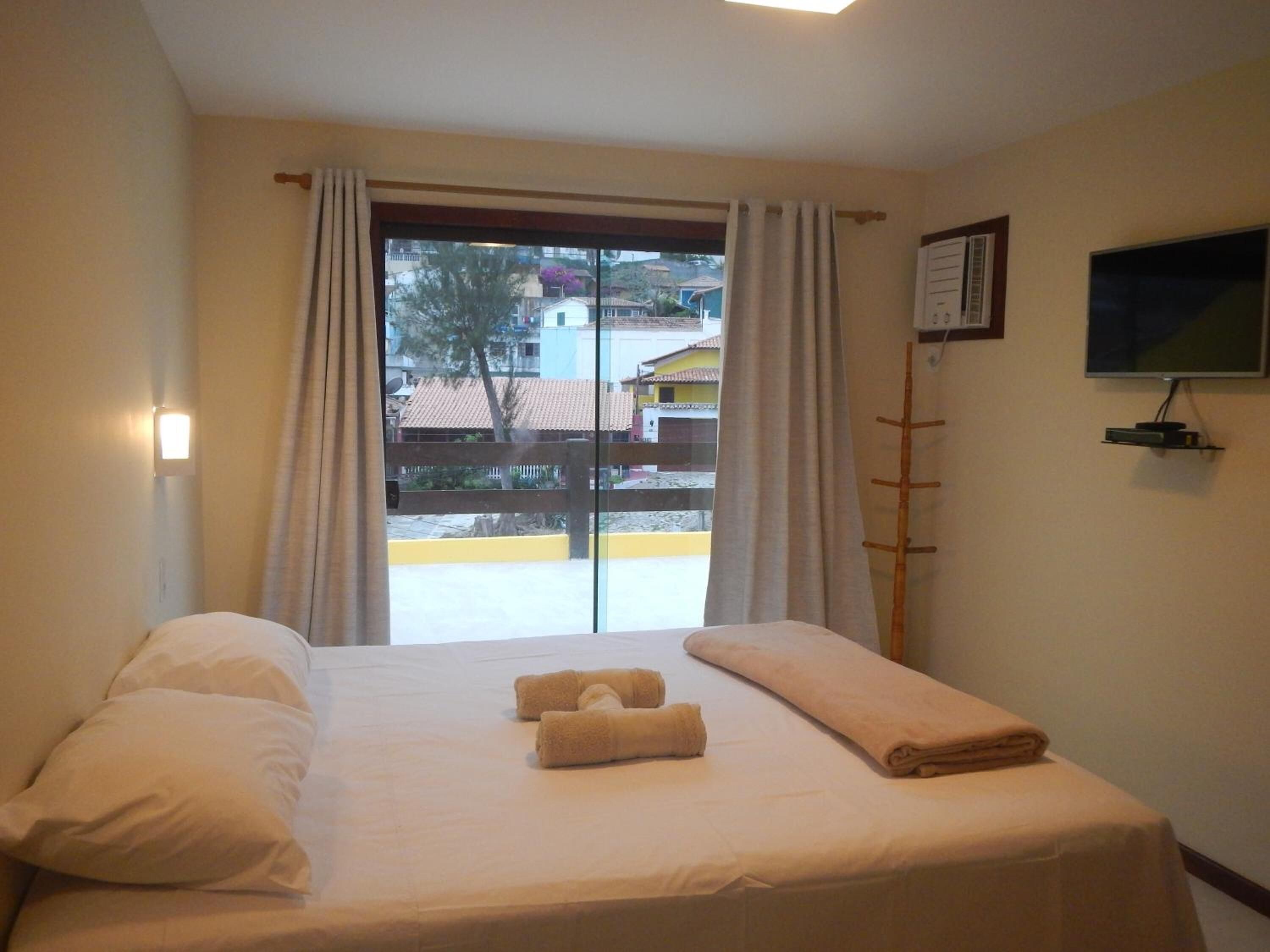 Una habitación de hotel con cama, dos toallas, televisión y ventana con cortinas.