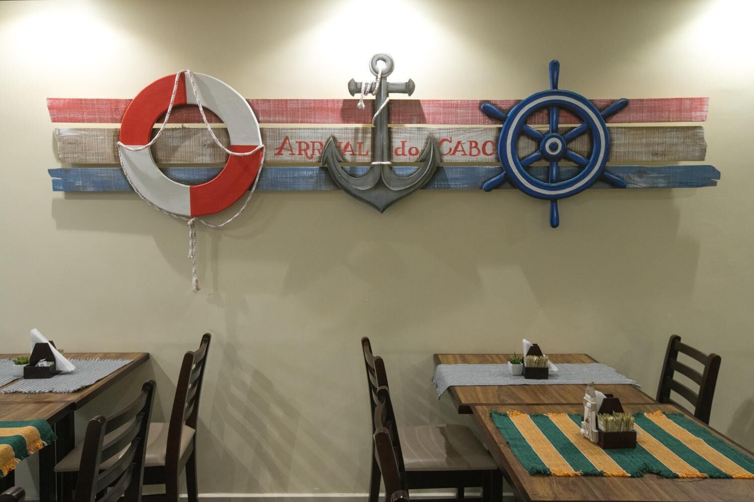 Un comedor con mesas y sillas de madera, y una decoración de pared con motivos náuticos.