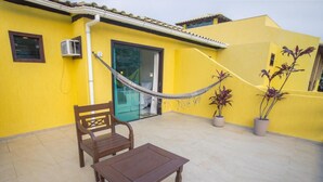 A yellow building with a hammock, a wooden bench, and potted plants. - Costa Dourada Pousada (Arraial do Cabo)