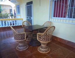 A dining area with a table and wicker chairs, a tiled floor, and barred windows.