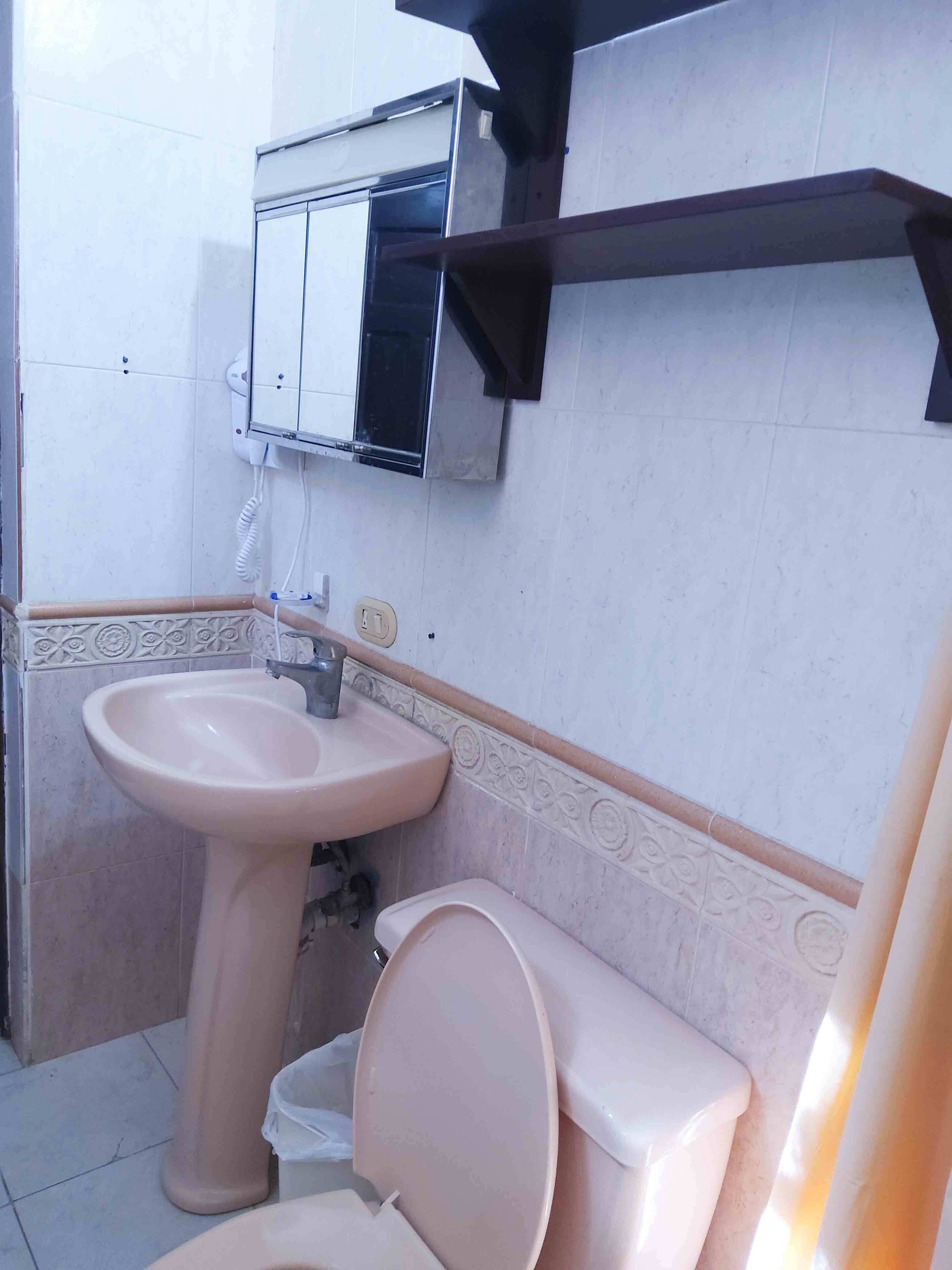 Un baño con lavamanos pedestal, inodoro y un armario sobre el lavamanos.