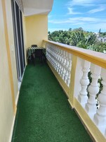 A balcony with artificial grass, a table with chairs, and a view of greenery and buildings.