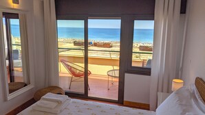 Een hotelkamer met een bed, een stoel en uitzicht op het strand en de zee.